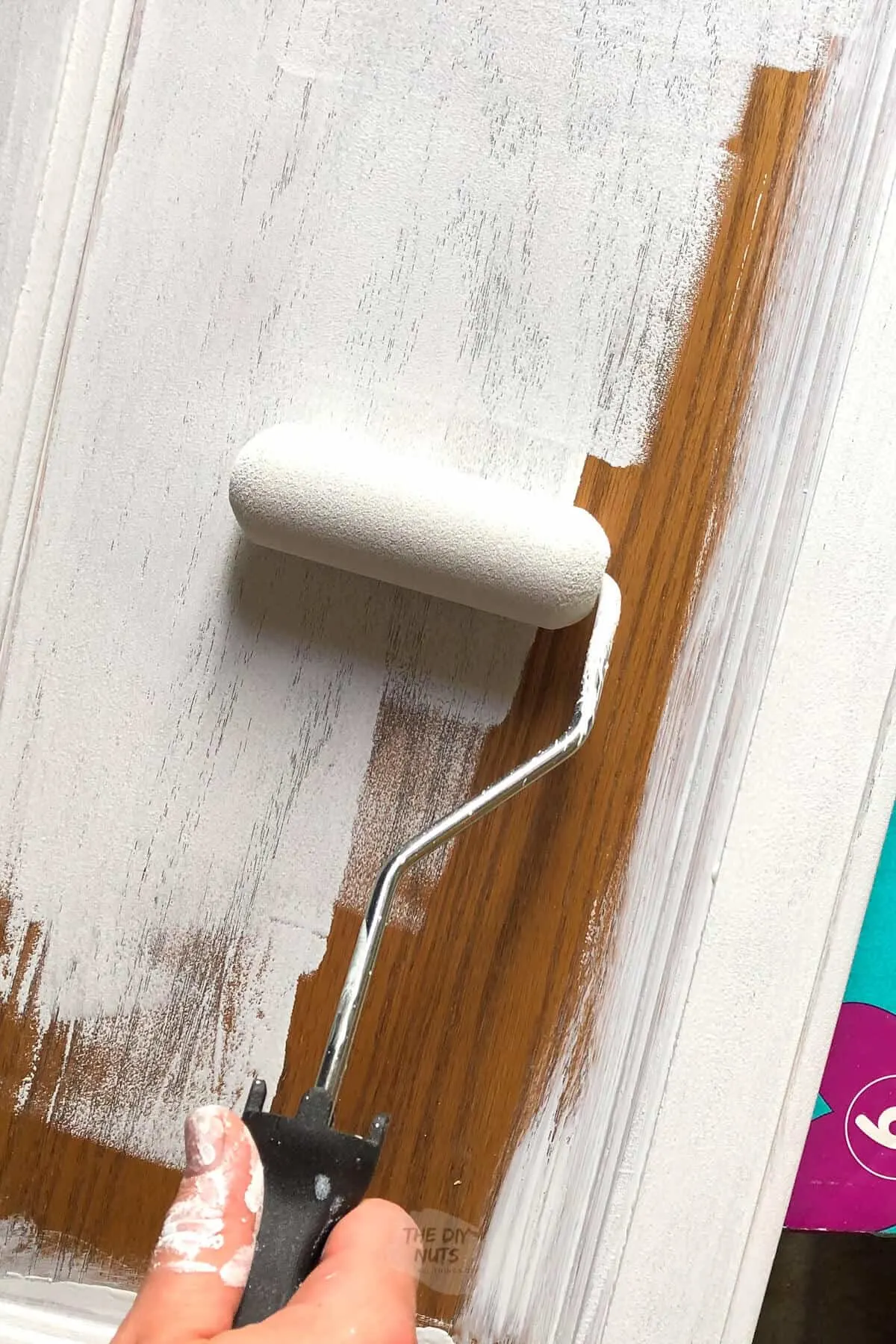 small foam roller applying latex primer to oak cabinet door.